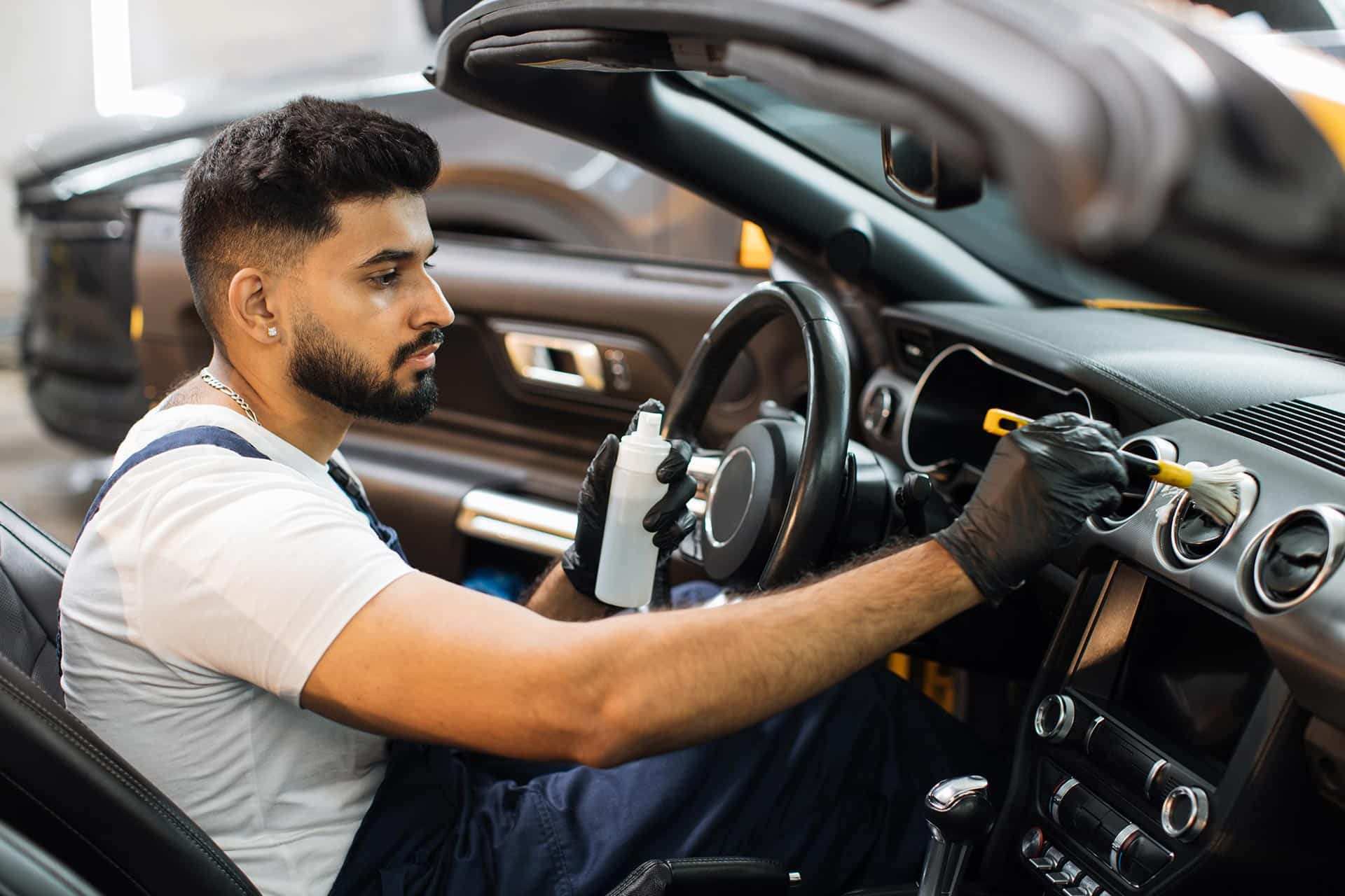 Professionnel nettoyant l'intérieur d'une voiture avec un spray et un chiffon.