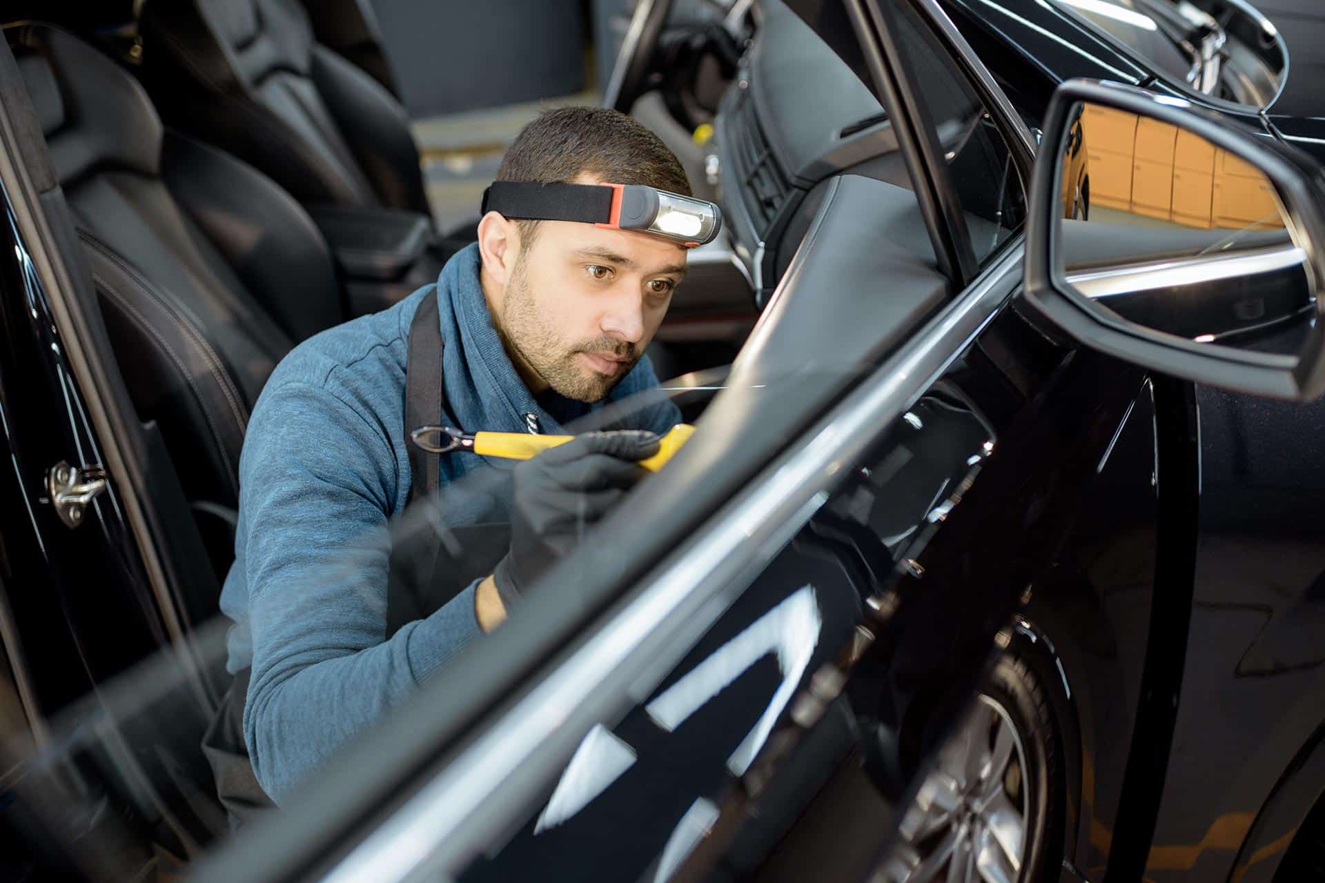 Mécanicien nettoyant minutieusement l'intérieur d'une voiture avec une lampe frontale.